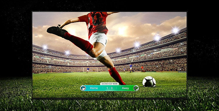 Hình ảnh màn hình chiếu một trận bóng đá với một cầu thủ mặc bộ đồ sọc màu đỏ chuẩn bị đá bóng ngang sân vận động. Điểm số trận đấu được hiển thị ở cuối màn hình. Thảm cỏ xanh từ sân trải dài ra ngoài màn hình đến phông nền đen.