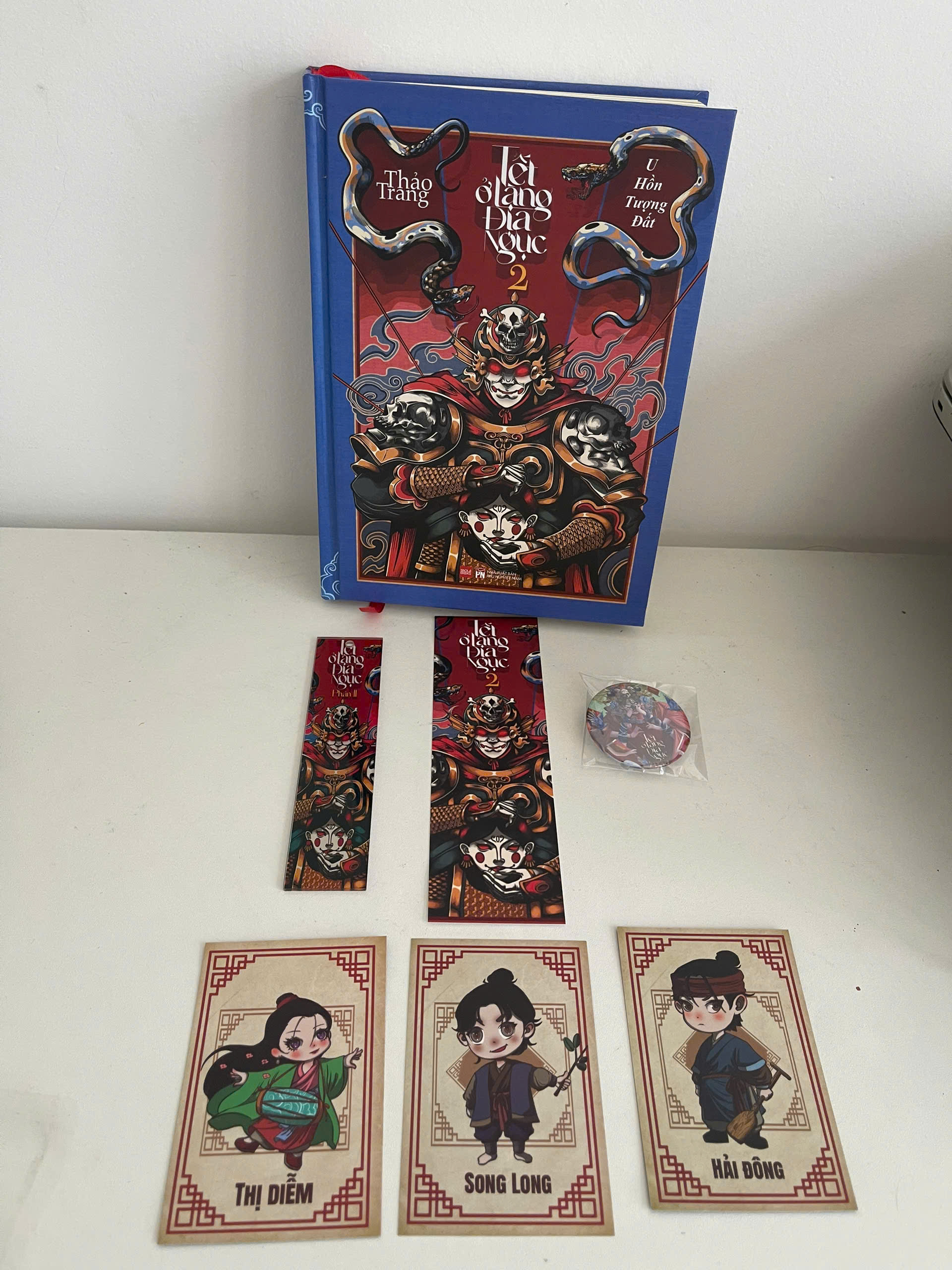 Sách - Tết Ở Làng Địa Ngục Phần 2 - U Hồn Tượng Đất - Saola Books - Thảo Trang - Bìa cứng - chữ ký tác giả - triện tên - bookmark giấy -bookmark mica - 3 thiệp chibi nhỏ - huy hiệu bìa sách