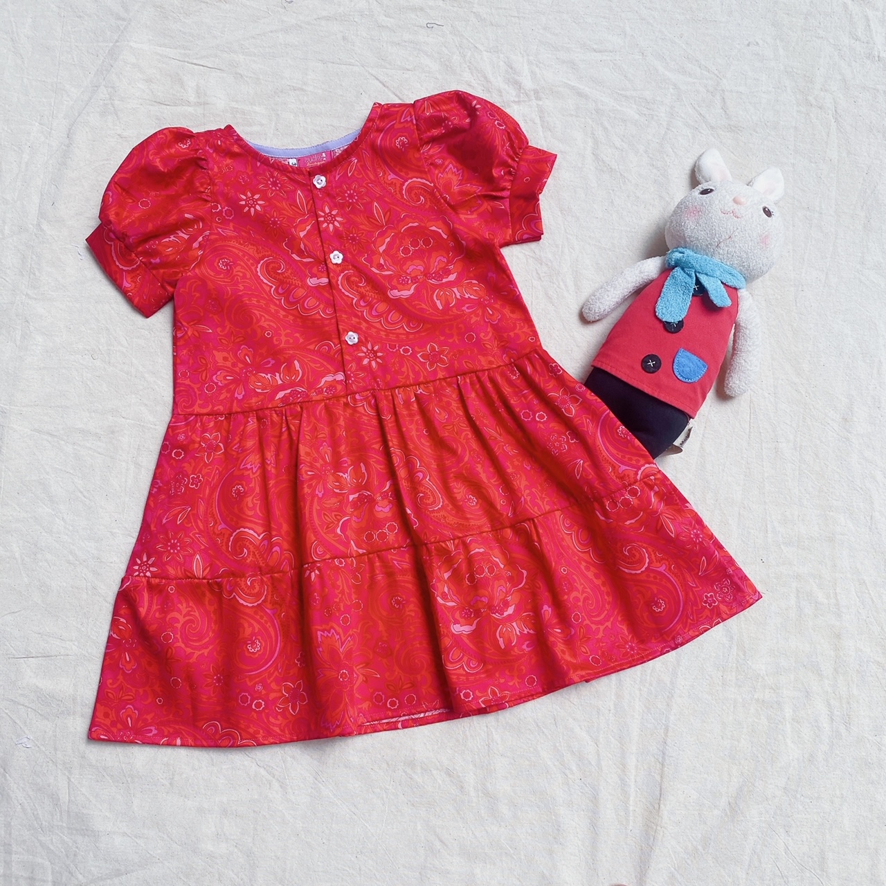 Đầm bé gái đỏ tay hồng gài nút trước