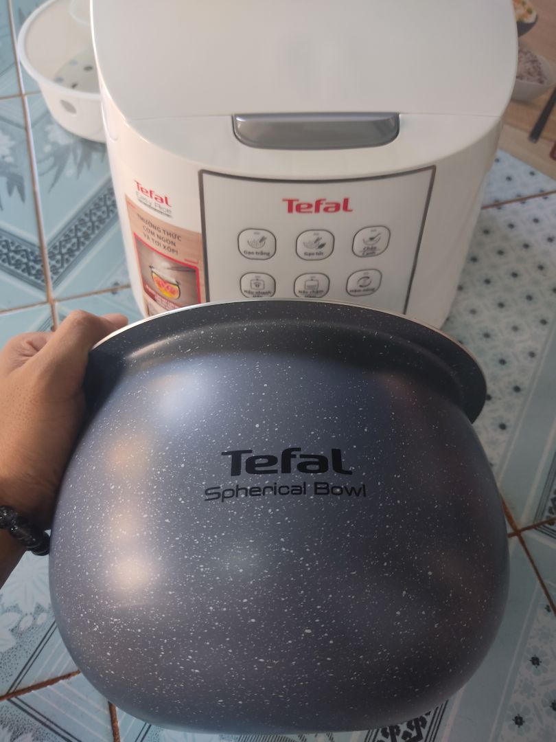 Nói về thương Hiệu Tefal là nói về sự hài lòng và an tâm về chất lượng rồi. Mẹ mình sử dụng rất chi là ưng luôn?. Sau khi sử dụng mình có một số đánh giá như sau:
+ Về thiết kế: Đẹp, sang trọng, màu trắng nhìn rất là đẹp luôn✨✨. Lòng nồi thì hình niêu tráng men nấu cơm không bị dính, không cháy, ngon cơm. Nồi không có tay xách nên một vài bạn đánh giá bất tiện, nhưng mình vẫn thấy nó có cái hay của nó, khi di chuyển nồi ta bưng bê, thay vì xách sẽ an toàn hơn và giúp nồi sử dụng được bền hơn.❤️. Một điểm khác biệt mà nếu để ý kĩ bạn mới biết là thành lòng nồi Tefal in cả logo của mình lên luôn, sang trọng hẳn lên, mình thấy các hãng khác không làm thế (chắc để tiết kiệm chi phí sản xuất). À mà ngoài xửng hấp và môi cơm như bao nồi cơm điện khác, Tefal còn tâm lý  cho khách hàng khi đi kèm thêm 1 môi múc cháo/canh nữa, yêu thế ???
+ Về chức năng: Có rất nhiều chức năng cho một nồi cơm điện với giá quanh 1 triệu đồng như thế này:  Gạo trắng, gạo lức, cháo/canh, nấu nhanh/hấp, nấu chậm/hầm, hâm nóng. Mình thì khoái chế độ gạo lức vì mình rất thích món sữa chua nếp cẩm ??Khi sử dụng chế độ nào thì nút sáng bật ở chế độ đó giúp người sử dụng rất dễ nhận biết. ❤️
+ Về khả năng giữ ấm: Nồi giữ nhiệt rất là lâu, nấu buổi trưa để đến chiều cơm vẫn còn ấm. Có thể là do nồi được thiết kế dạng niêu nêu mới hỗ trợ giữ ấm lâu như vậy.❤️Thêm vào đó ron cao su ở phần nắp rất dày, dẻo đảm bảo hơi được giữ kín như bưng trong nồi nữa
+ Về quà tặng: Theo mình nghĩ với mức giá đã giảm chưa tới 1 triệu là quá ok cho một nồi cơm điện Tefal như thế này rồi, nhưng Tefal lại còn tặng thêm 1 chảo chống dính có tem đỏ báo nhiệt, thành chảo cao giúp hạn chế bị bắn dầu mỡ khi chiên xào thì lại quá là xuất sắc luôn. 
Nói tóm lại là quá nên mua mọi người ạ. Mình đã tin mua và cả nhà mình rất hài lòng về Tefal