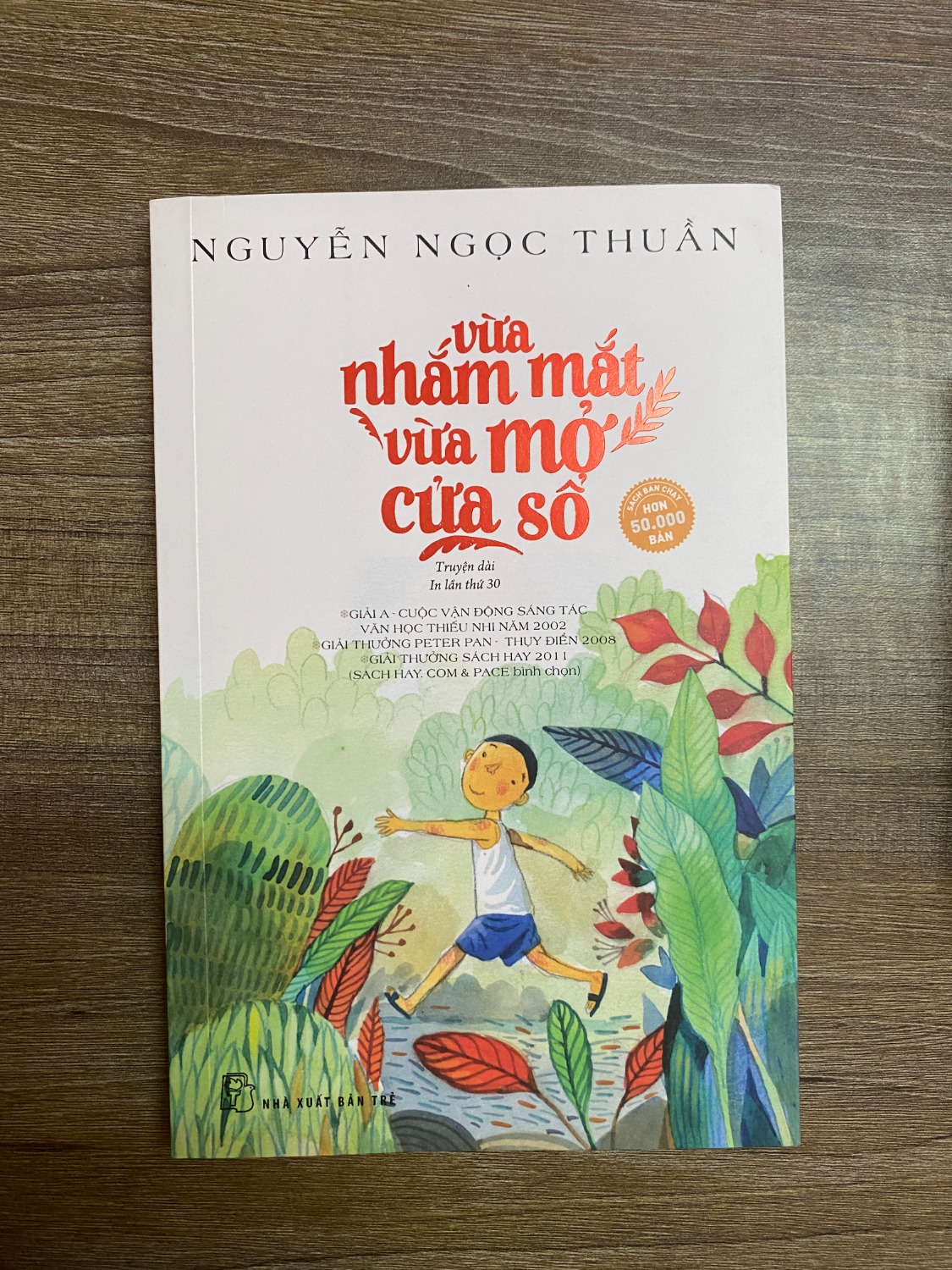 Cuốn "Vừa nhắm mắt vừa mở cửa sổ" in lần thứ 30 của NXB Trẻ có khổ vừa, dày gần 200 trang và có bao gồm một số hình minh hoạ khá trừu tượng. Sách có bao gồm nhận xét của một số nhà văn Việt Nam và bản dịch một đánh giá của một blogger nước ngoài.

Tóm tắt: "Vừa nhắm mắt vừa mở cửa sổ" là một truyện dài, chứ không phải là một tập truyện ngắn dù mỗi chương đều có tiêu đề riêng và hoàn toàn có thể đứng riêng rẽ mà không ảnh hưởng đến cấu trúc câu chuyện. Truyện được kể bởi nhân vật "tôi", một chú bé 10 tuổi, về những cảm nhận của cậu về thế giới xung quanh. Dưới con mắt trẻ thơ trong veo, từng chi tiết hiện lên một cách rất ngoạn mục. Từ chuyện cái răng khểnh của bản thân, đến tình yêu của cô chú hàng xóm, hay là những bí mật nho nhỏ với cô giáo, bố mẹ, bạn bè...

Tác phẩm thực sự là một huyền thoại văn học Việt Nam. Nó đã được tái bản nhiều lần và dịch sang nhiều thứ tiếng khác nhau, và đọc rồi mới thấy nó không ngoa chút nào. Mình đọc cuốn này lần đầu khi mới rời giảng đường đại học, tức là ở độ tuổi không phải người lớn, cũng chả phải trẻ con, mà lại đọc bản dịch tiếng Anh, nên khi đó không thực sự hiểu được cái đẹp của tác phẩm như bây giờ.

Cái đẹp của tác phẩm không chỉ đến từ giọng văn ngây thơ, trong sáng của một đứa trẻ 10 tuổi mà còn là sự mô tả tài tình về góc nhìn thú vị của trẻ con. Đọc tác phẩm này, mình chợt nhớ ra mình cũng như vậy khi còn là một đứa trẻ. Cũng nhìn từng cành cây hoa lá, từng con vật, từng người xung quanh với những suy nghĩ bay bổng và mộng mơ. Hoá ra, đứa trẻ nào cũng vậy, khi bắt đầu biết cảm nhận thế giới, cũng thấy bao điều thú vị, cũng thấy trí tưởng tượng của mình bồng bềnh bồng bềnh..

Một điểm thú vị nữa của tác phẩm mà rất nhiều người đã chỉ ra, đó là người lớn đọc tác phẩm này cũng rất hợp. Hợp là bởi vì những bài học có thể rút ra được từ mỗi chương trở lên rõ ràng khi bạn là người lớn. Như là sự tự tin với khiếm khuyết trên cơ thể mình, như là tình yêu thương đồng loại, hay đơn giản chỉ là việc ăn năn biết lỗi. Ngoài ra, mình cũng thấy bậc làm cha làm mẹ sẽ học được nhiều điều từ cuốn sách này. Các nhân vật bố, mẹ, cô, chú, cô giáo,... trong truyện đều hết mực bảo vệ cậu bé khỏi những phũ phàng của cuộc sống trưởng thành và luôn để cậu sống vô tư với tuổi thơ mộng mơ của mình. Điều đó chính là quà tặng lớn nhất phụ huynh có thể dành tặng cho các em.

Trích dẫn hay: "...khi một ai đó buồn, họ cần rất nhiều người để chia sẻ. Nỗi buồn chỉ vơi đi bằng tình thương chứ không có một phương thức nào hết. Khi chia sẻ một nỗi buồn, chúng ta sẽ không buồn hơn, nhưng người khác lại vui hơn. Và đừng bao giờ quay lưng lại với một con người như vậy. Họ cần những khuôn mặt hơn là những viên thuốc. Họ cần những bàn tay, những tô cháo, những quả ối hái để đầu giường. Họ cần mỗi buổi tối ghé lại ngồi với họ trong im lặng. Họ cần chúng tả dẫn họ lên đồi cuốc một mảnh vườn, và thỉnh thoảng hỏi có thích ăn bắp rang không..."

Điểm đánh giá cá nhân: 5/5