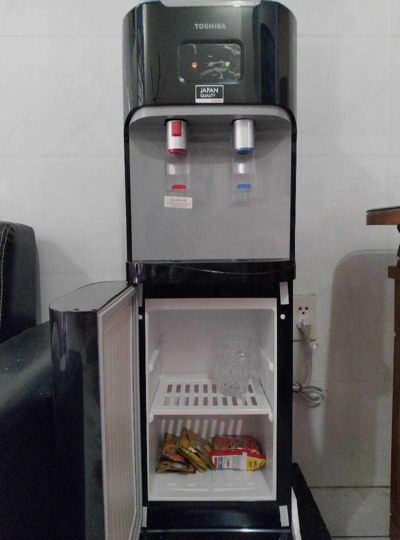 Đặt sáng hôm nay, Tiki sáng hôm sau giao ngay dù là ngoại thành. Máy mới còn niêm phong, mẫu mã đẹp, sang, phụ kiện giấy giờ đầy đủ.
Cho những ai mới lần đầu dùng cây nóng lạnh như mình (hướng dẫn mình đọc từ tờ giấy hãng kèm theo). Setup máy ở chỗ thoáng mát. Trước khi cắm nguồn, phải nối dây max (dây tiếp đất). Lắp bình nước, đợi nước lấp đầy bình nóng và bình lạnh ( lúc chổng bình vào nó sẽ ọc bọt khí, hết bọt khí là chăm đầy ). Lấy ly nước mở thử coi 2 vòi ra nước chưa (riêng vòi nóng có nút khoá an toàn phải vừa ấn nút vừa đẩy vòi nước mới chảy ra) Đợt nước đầu này sẽ có mùi nhựa do mới nên sẵn bỏ luôn. Khi đảm nước đầy đủ thì mới cắm điện và bật công tắc nóng, bật công tắc lạnh bên hông lên. Bạn chịu khó chờ nó làm nóng 15p, còn lạnh tầm 2 tiếng chưa tới. Độ nóng phù hợp uống trà cà phê ăn mì, còn lạnh thì tạm thôi, cỡ ngăn mát tủ lạnh chứ không hơn. Khi làm nóng hay lạnh xong thì đèn báo mới tắt, để ngưng sử dụng và tiết kiệm điện. Máy chạy đầm êm, ưng em ngăn mát đựng đồ khá tiện dụng!